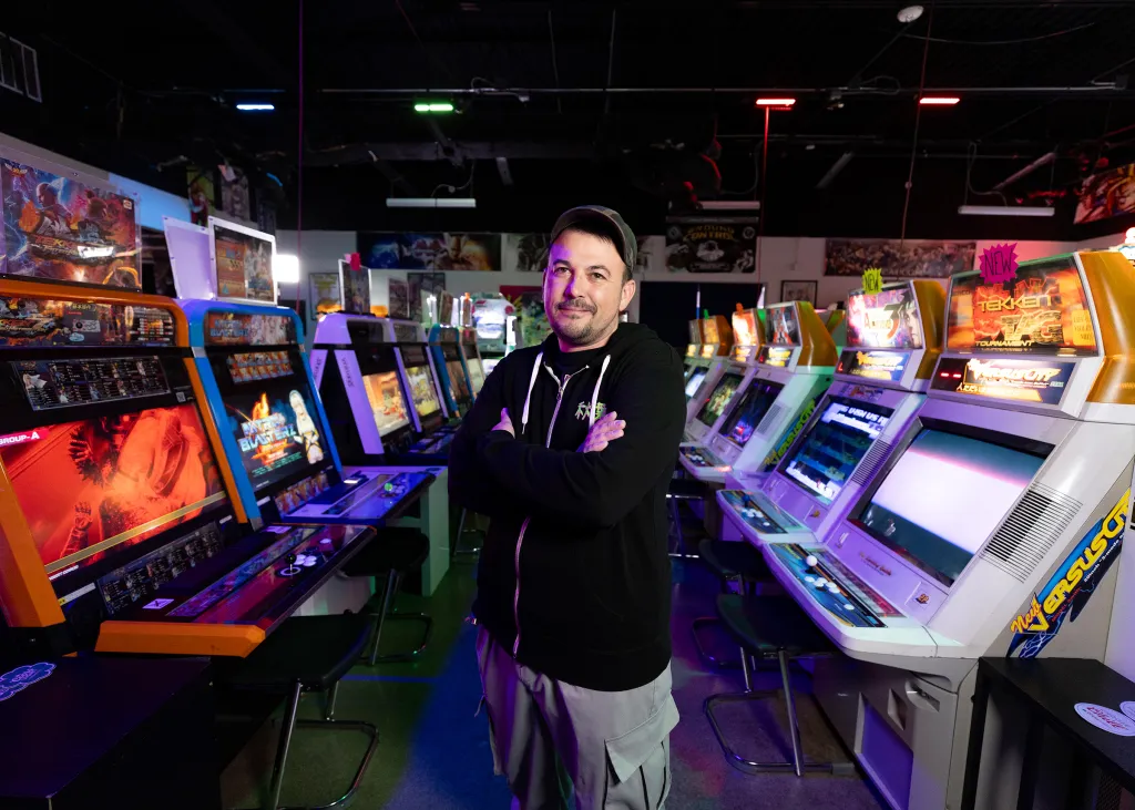 Man standing with his arms crossed in front of a row or arcade games