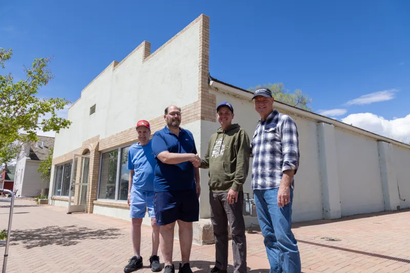 4 men standing outside of the Rodeo Building with 2 of them shaking hands