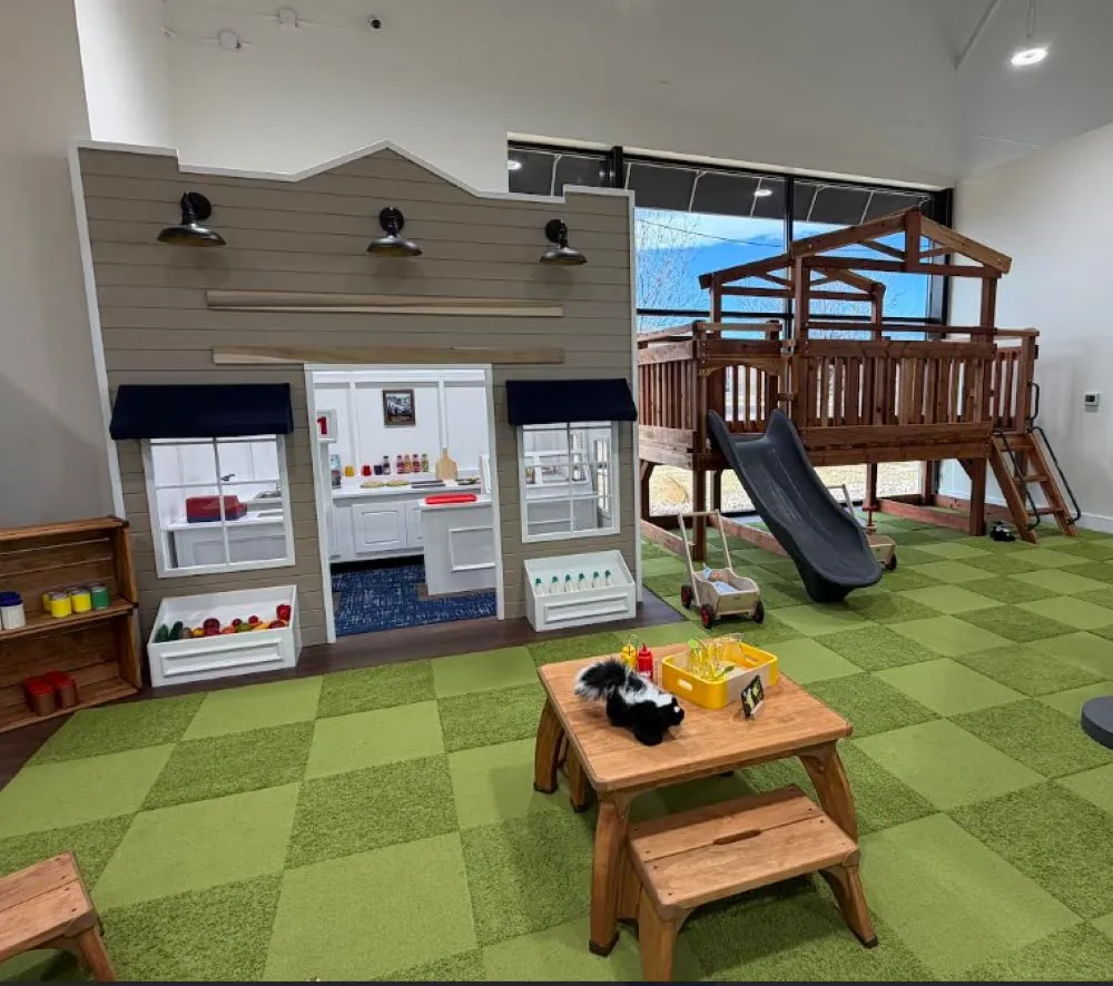 Indoor kids play area with a small storefront a wooden play area, table bench and green floor tiles