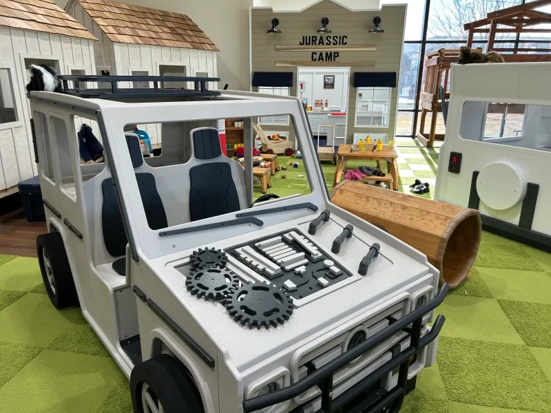 Indoor kids play area with child sized storefronts, a jeep to sit in and tables to sit at