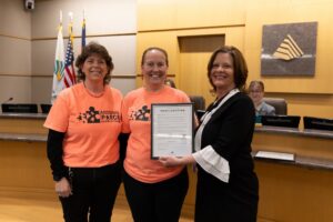 Person holding a framed document taking a photo with two business owners