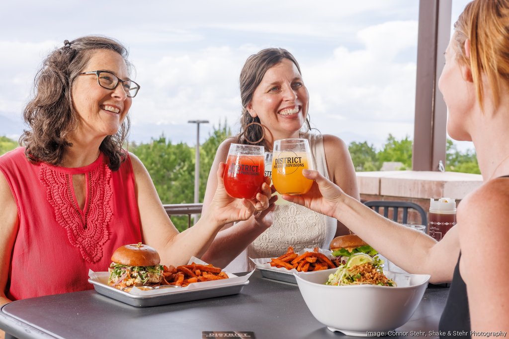Three people at a table eating food and doing a cheers with 3 drink glasses that say District Pour