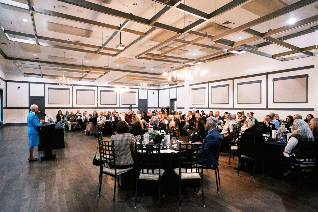 People sitting at tables in a room with a speaker at a podium in the front